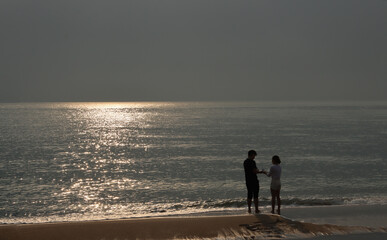 the silhouette of a couple standing on the sandy beach by the sea