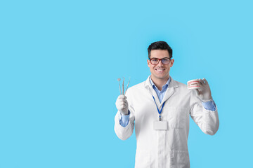 Male dentist with plastic jaw model and tools on color background