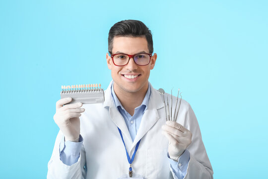 Male dentist with plastic teeth color samples and tools on color background