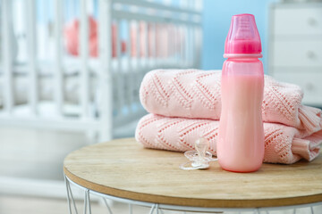 Bottle of milk for baby with pacifier and clothes on table