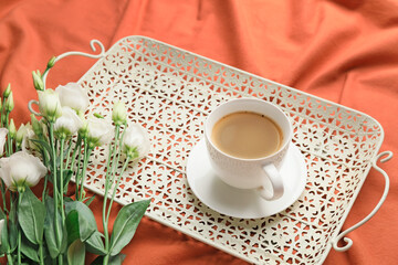 Tray with cup of coffee and flowers on bed