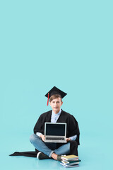 Male graduating student with laptop on color background