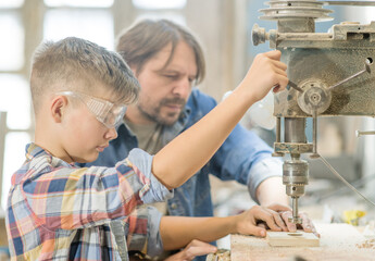 Man teaches the boy to work on the drilling machine in the carpentry workshop
