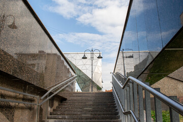 Fototapeta premium Stone or concrete staircase, ladder leading up to the city. Glass mirror arch in modern style. Summer day. Walking alley. Modern figure abstraction. lamppost