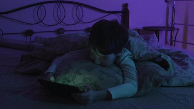 Boy Caught By His Parents Using The Phone At Night. Schoolboy Laying In Bed Holding Cellphone Staring At Mobile Phone Screen Smartphone Addiction Concept