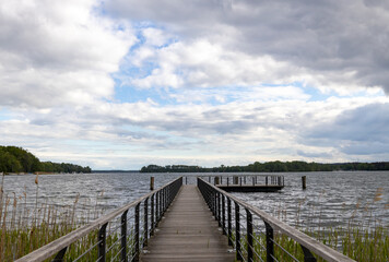 Fototapeta na wymiar a long wooden jetty by a lake. a bright blue sky with many clouds in the sky.