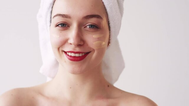 Makeup foundation. Cosmetic product advertising. Beauty care. Happy smiling woman in white towel applying smudging beige spf protection CC or BB face cream on skin with fingers.