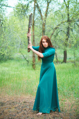 Young woman in elegant dress with cudgel in hands. Lady in spring forest. Danger and self-defence...