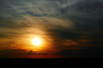 beautiful sunset sky, bright sun and dark silhouette of clouds as a background