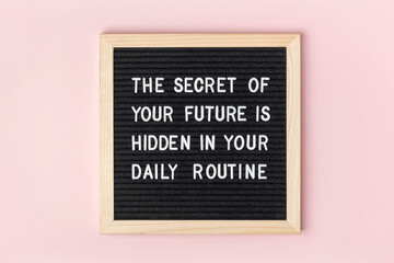 The secret of your future is hidden in your daily routine. Motivational quote on black letter board on pink background. Concept inspirational quote of the day. Greeting card, postcard
