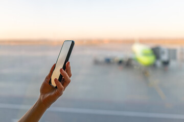 Close-up shot of female hand holding smart phone by window at airport. Area with airplane in background