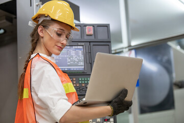 Factory worker is programming a CNC milling machine with a tablet computer. engineering and worker woman in safety hard hat and reflective cloth using lathe machine inside the factory.