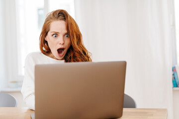 Young woman staring wide eyed at her laptop computer
