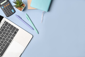 Laptop computer, calculator, notebook and pens on blue pastel background.