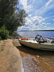 Fototapeta na wymiar old motor boat on sandy shore with beautiful green summer landscape