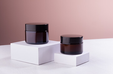 Cosmetic mockup -  jars for cream of amber glass with black caps on white podiums. Template for...