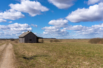 Fototapeta na wymiar An old abandoned small wooden house in the field blue sky white clouds, barn or scary concept.