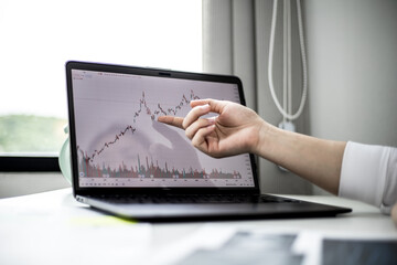 A stock investor is pointing to a laptop screen running a stock chart program to read stock price charts, analyze purchases. Cryptocurrency stocks are popular with both new and old investors.