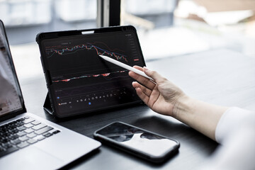 Stock investor holding a pen pointing a tablet screen that opens a stock chart program to read...