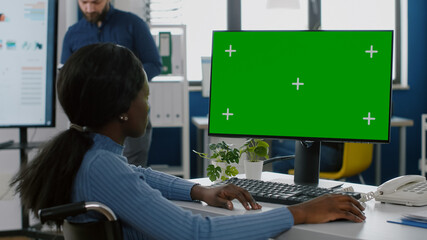 African disabled invalid handicapped businesswoman sitting in wheelchair analysing financial statistics, looking at pc with green screen chroma key mock up izolated desktop planning business project