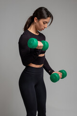 Sporty girl performing bicep curl with dumbbells on grey background