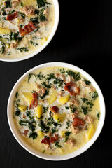 Homemade Zuppa Toscana with Kale and Bread in a white bowl on a black surface, top view. Overhead, from above, flat lay.