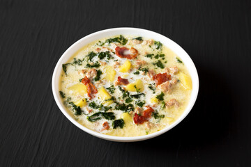 Homemade Zuppa Toscana with Kale and Bread in a white bowl on a black background, side view.