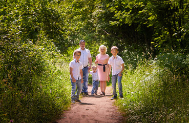 Fun walk of large family in the summer forest. Mother, father, brothers walking in the park or forest on a sunny day