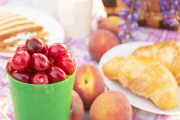 Juicy cherries, croissants, peaches, sandwich on a pink checkered tablecloth