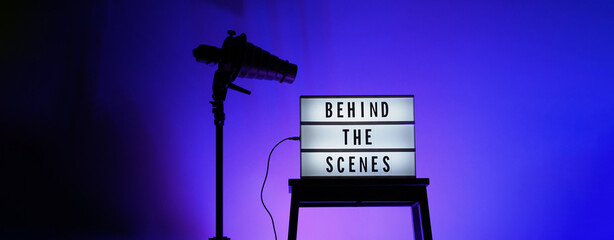 Behind the scenes letterboard text on Lightbox or Cinema Light box. Movie clapperboard megaphone and director chair beside. Background LED color change loop. static camera in video production studio.