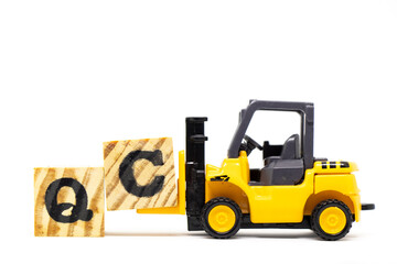 Toy forklift hold letter block c to complete word QC (Abbreviation of Quality Control) on wood background