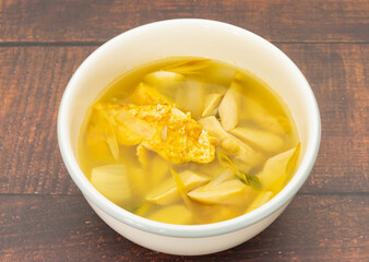 Soft tom yum soup with omelet, mushroom, galangal, lemongrass in white bowl on wood table