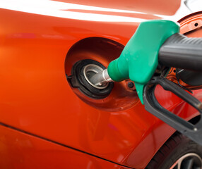 Green benzene gas pump nozzle filling up orange sport car tank. Close up