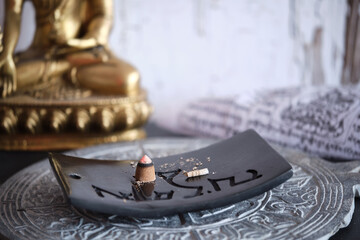 Tibetische Räucherkegel auf schwarzem Specksteinhalter mit goldenem Buddha (Close-up)