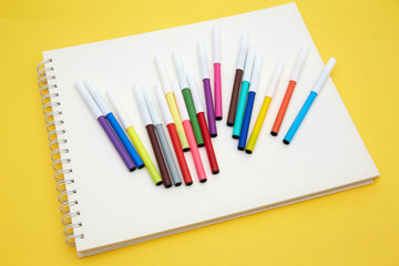 Top view of multicolored pointed markers on white sketch book  isolated on yellow background