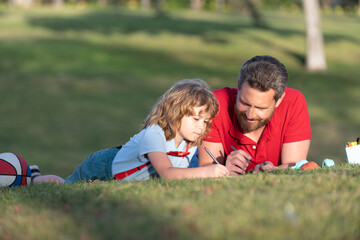 father and son relax on grass in park learning to draw, fatherhood