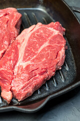 A raw marbled beef steak sits in a frying pan.