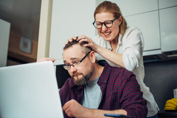 Bearded man and woman with eyeglasses using laptop in the home interior, communicate with friends online, laugh and grimace.