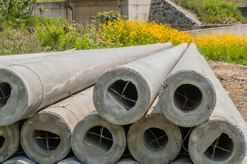Closeup of ends of utility poles laying on ground with yellow flowers in background.