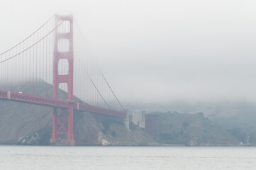 Fototapeta premium The red structure of the golden gate bridge in the fog, San Francisco, California, USA. White sky, with copy-space.