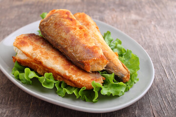 Fried pollock fish on a plate with salad leaves on an old wooden background