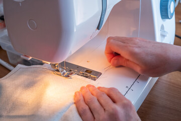 Unidentifiable seamstress sewing with an electric sewing machine with selective focus, shallow depth of field and bokeh