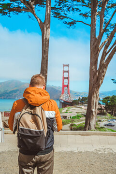 Rear view of a young man in a jacket admiring the Golden Gate Bridge in San Francisco on a sunny day