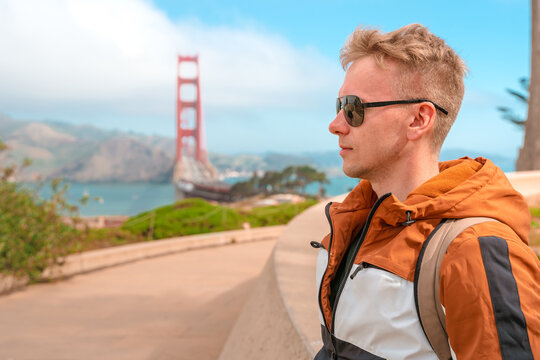 A young man walks along the boardwalk overlooking the Golden Gate Bridge in San Francisco on a sunny day