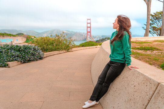 A cute young brunette woman walks on a hill overlooking the Golden Gate Bridge in San Francisco on a sunny day