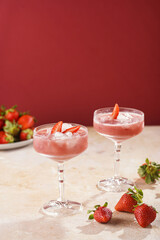 Two glasses with red strawberry dessert with ice cubes and crashed ice and strawberry slices on...