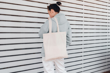 Pretty woman in hoodie with white cotton bag on her shoulder. Mockup and zero waste concept.