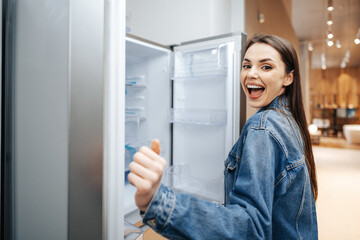 Young attractive woman choosing refrigerator in hypermarket