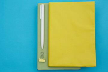 Top view of green and yellow book and white pen isolated on blue background 