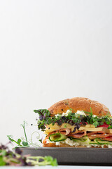 Bun with sausage, cheese and cucumbers, microgreens and mozzarella and radishes, delicious hearty burger close-up on a plate cooked at home